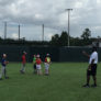 Athletes hold bats on turf and coach explains hitting focus